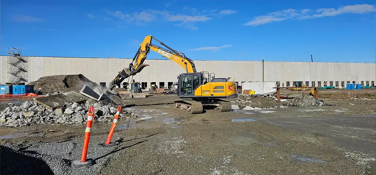 Excavator demolishing concrete beside a tilt-up building