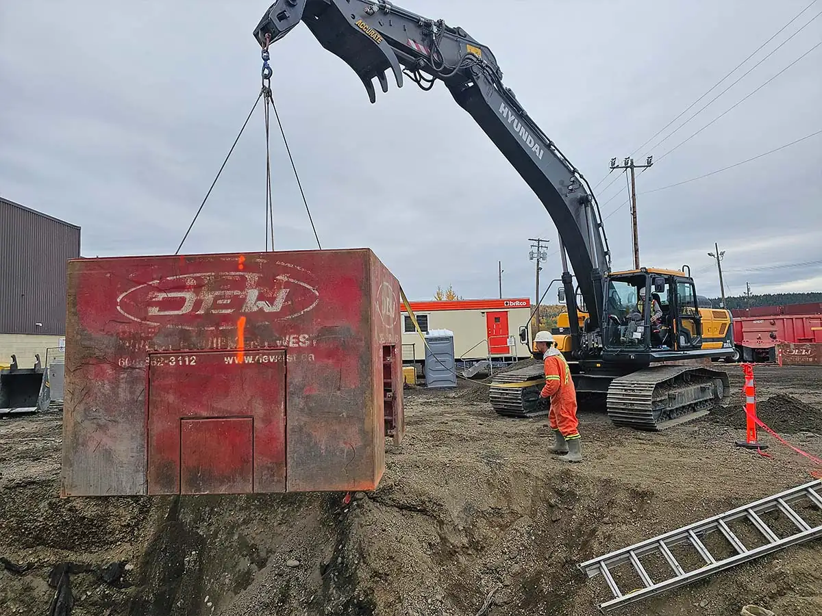 Excavator lowering a trench box into a utility excavation