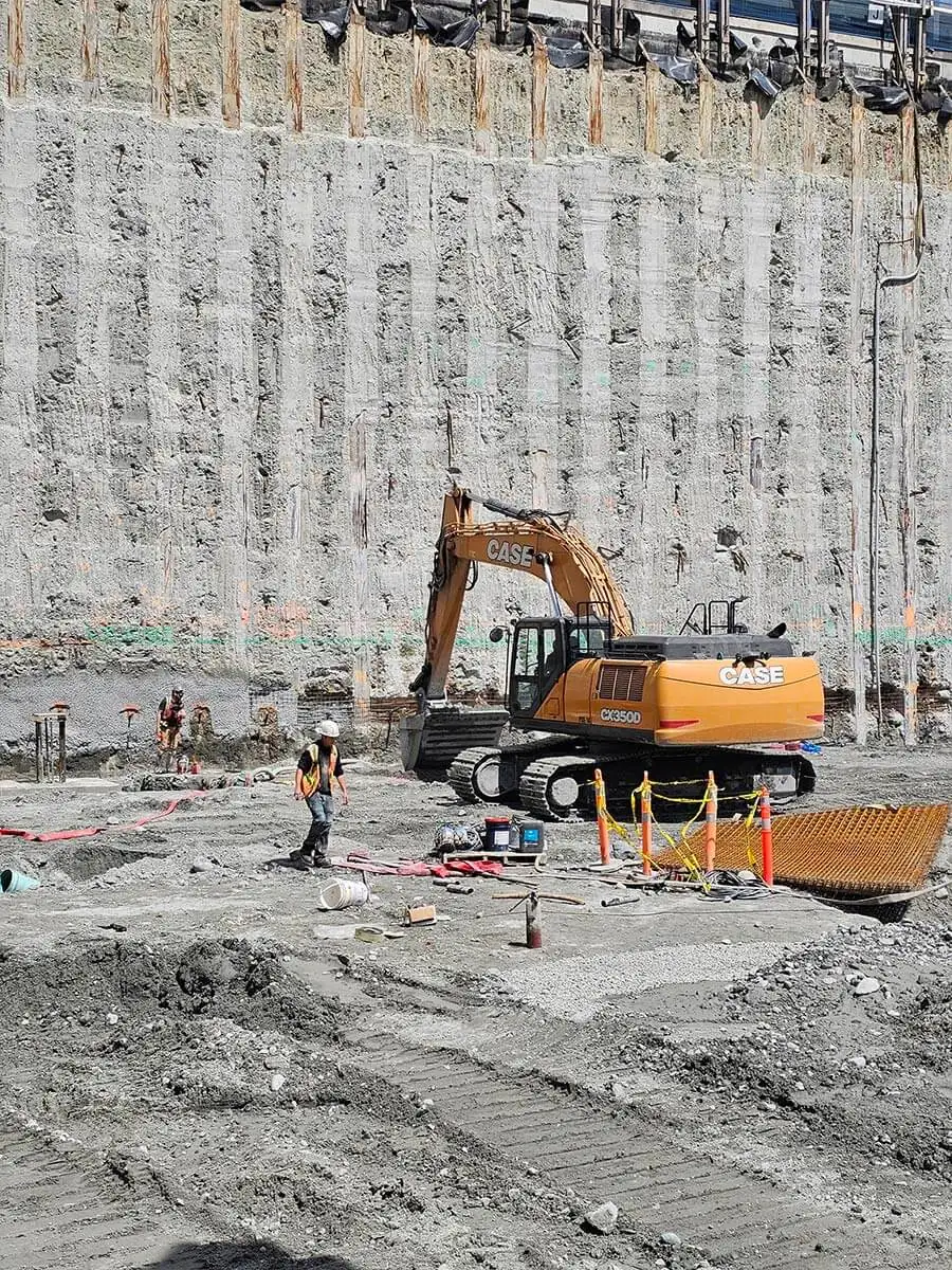 Excavator at the base of a shotcrete shoring wall
