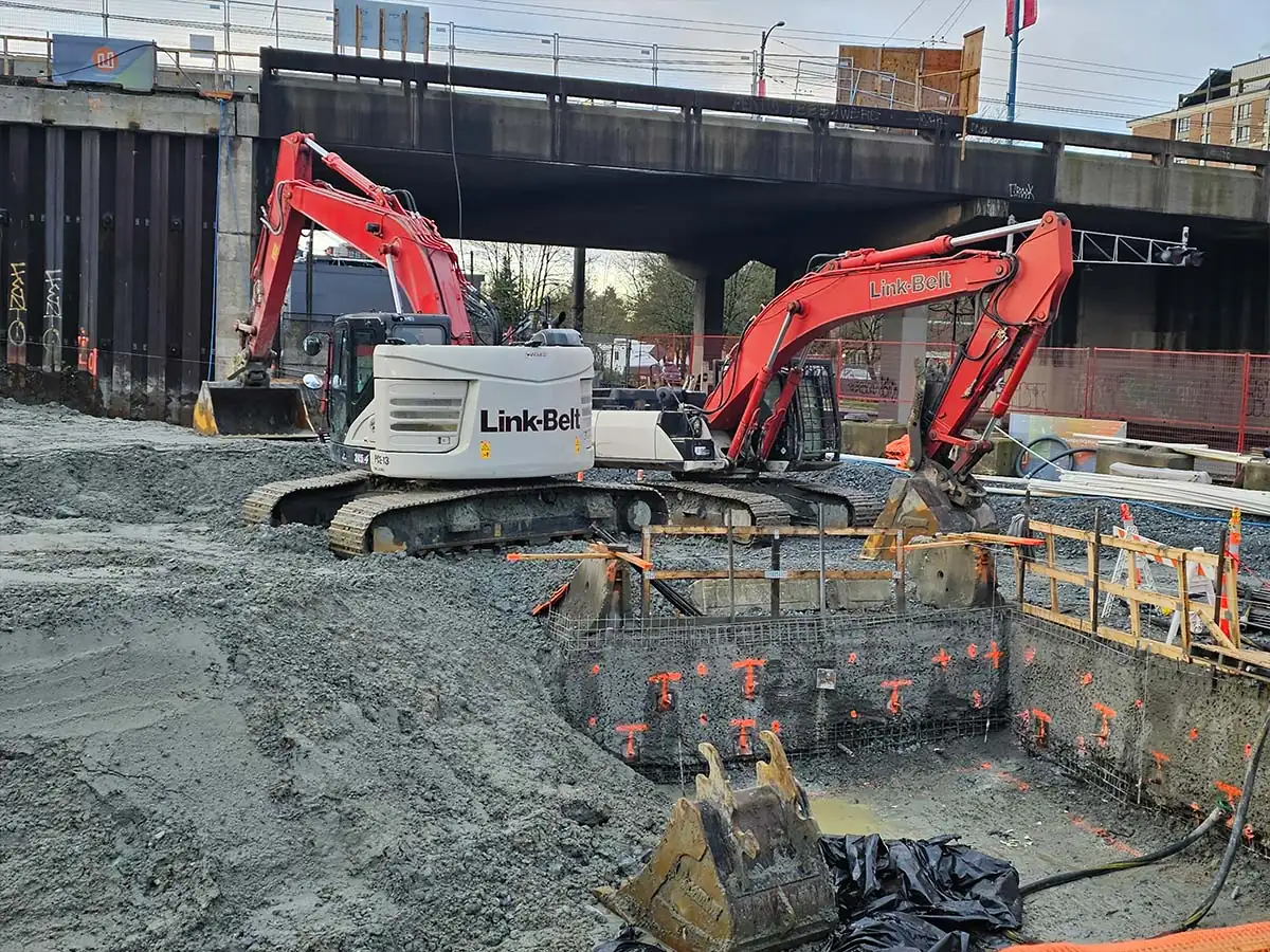 Two excavators in a commercial excavation beside a rail line