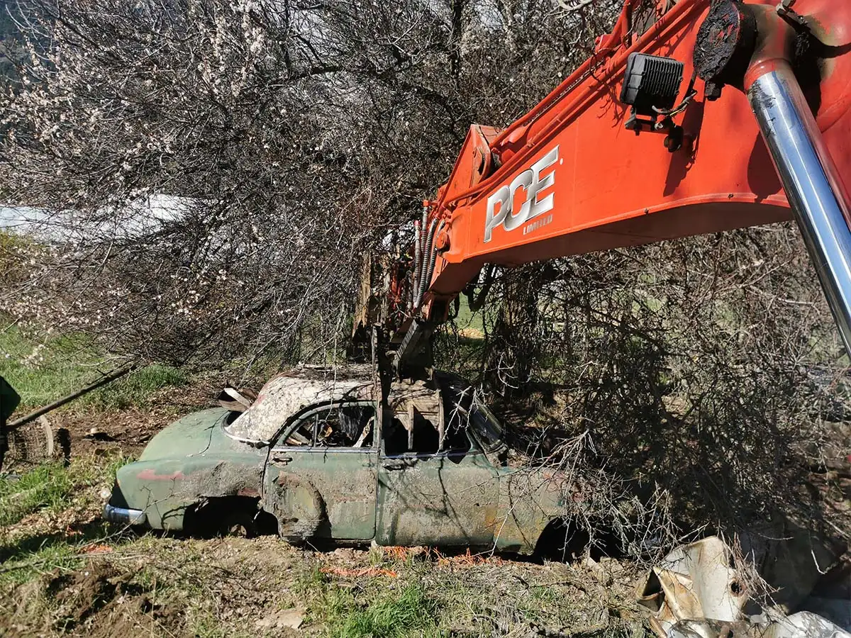 PCE excavator lifting a derelict car from brush on a hillside