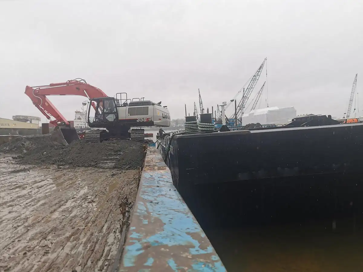 Excavator loading excavated material onto a barge at the dock