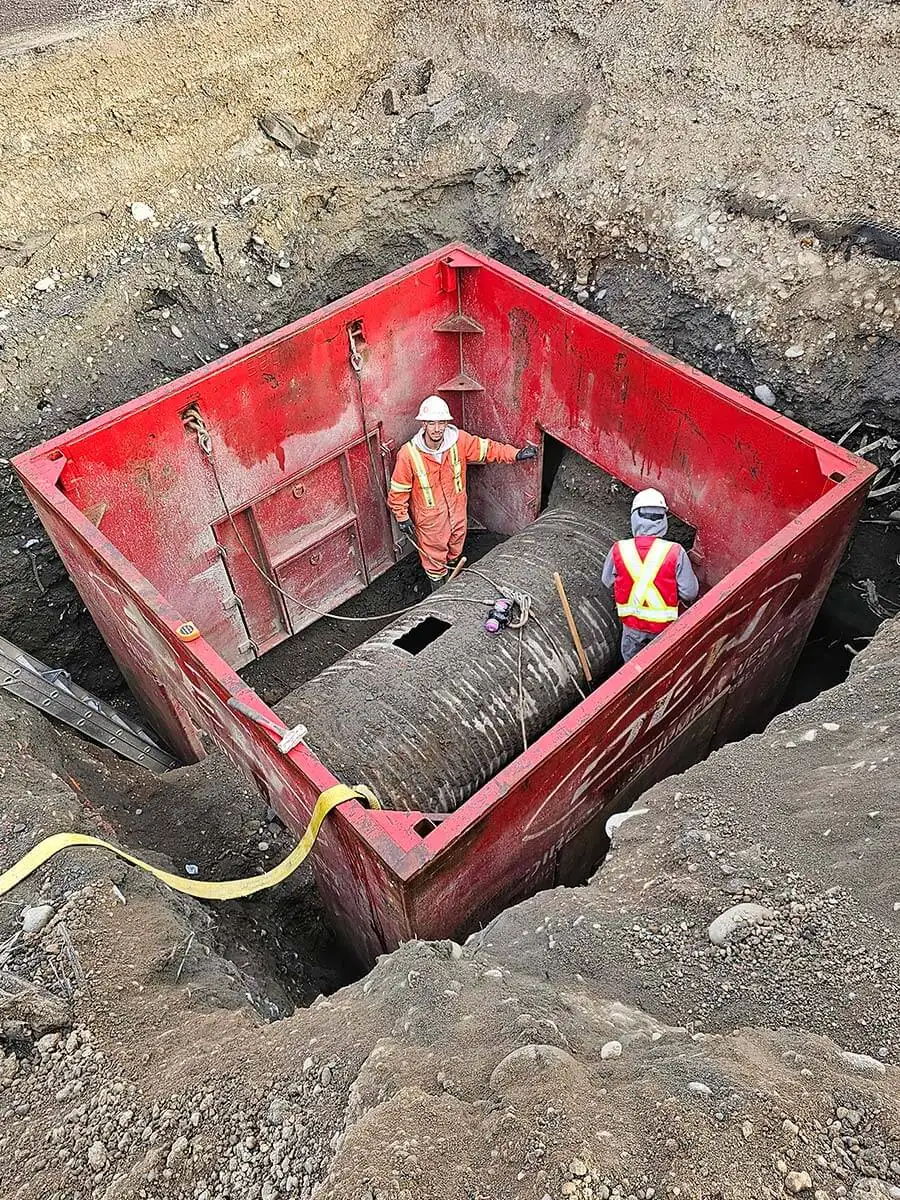 Crew working inside a large shoring box around a pipe fitting