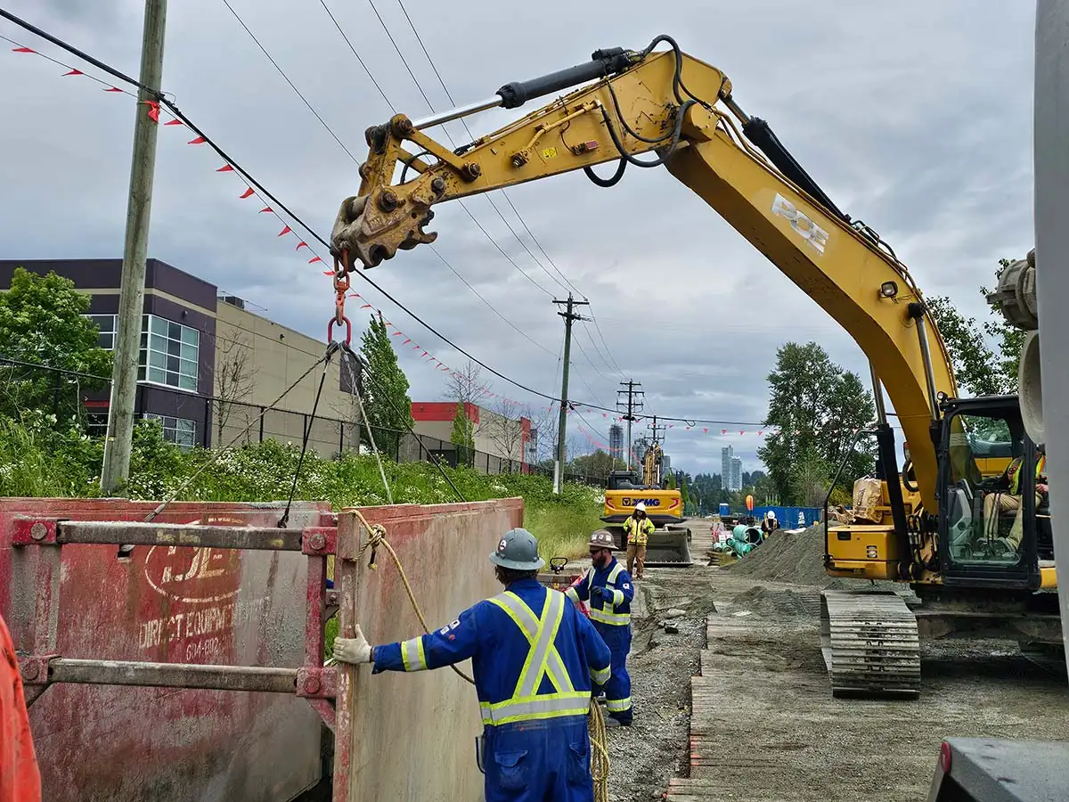 Excavator setting a trench box beside the road