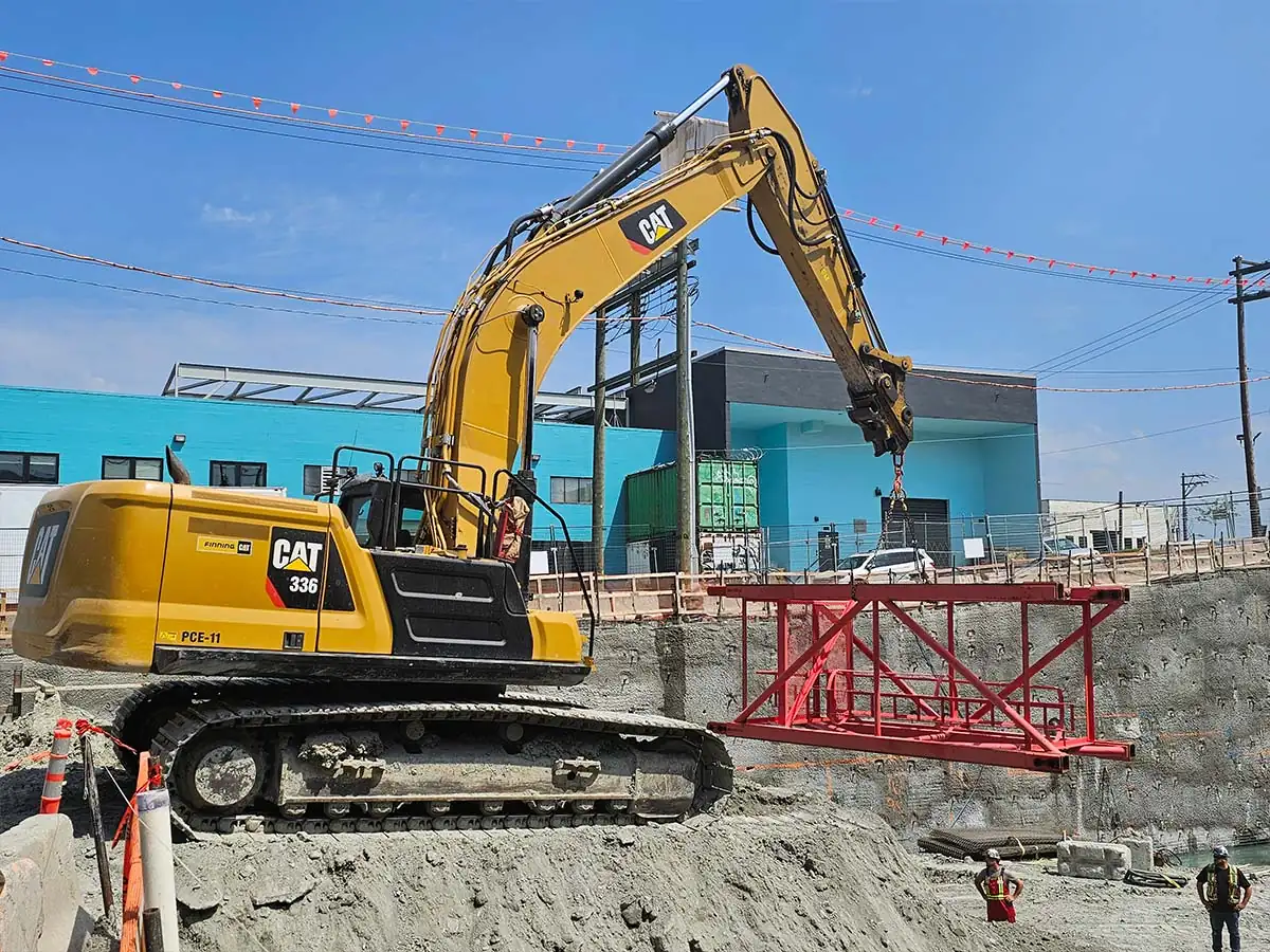 Excavator at the edge of a shored excavation beside an urban street